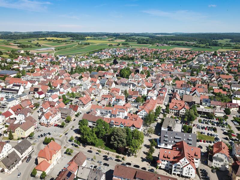Eine Luftaufnahme zeigt eine Stadt mit roten Dächern, umgeben von Feldern und Wäldern.