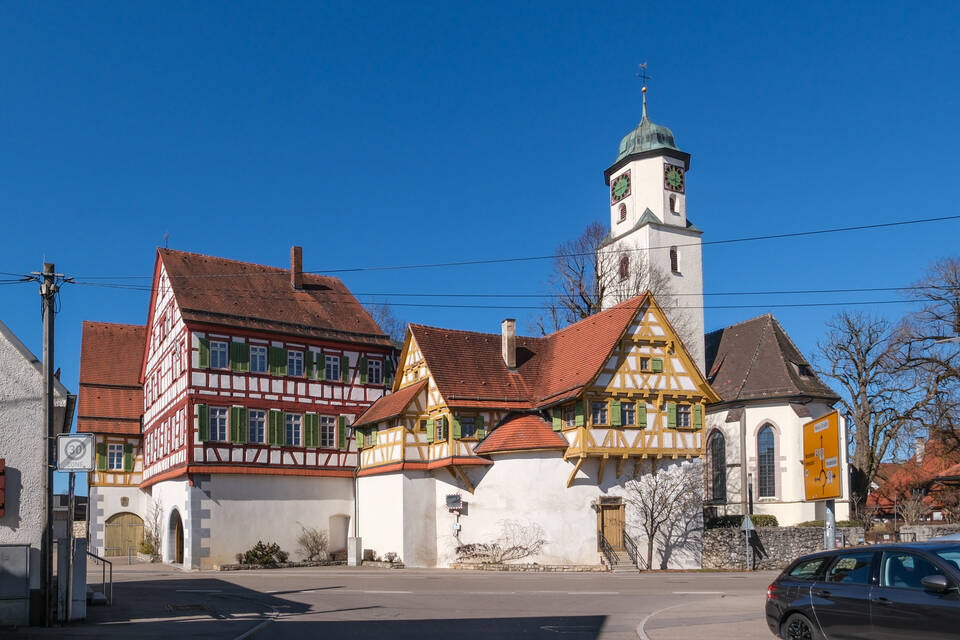 Die malerische Laichinger Kirchenburg und eine Kirche mit einem Glockenturm stehen nebeneinander unter klarem blauem Himmel.