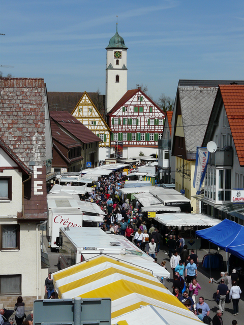 Bild einer belebten Innenstadt mit einem Markt und Kirche im Hintergrund
