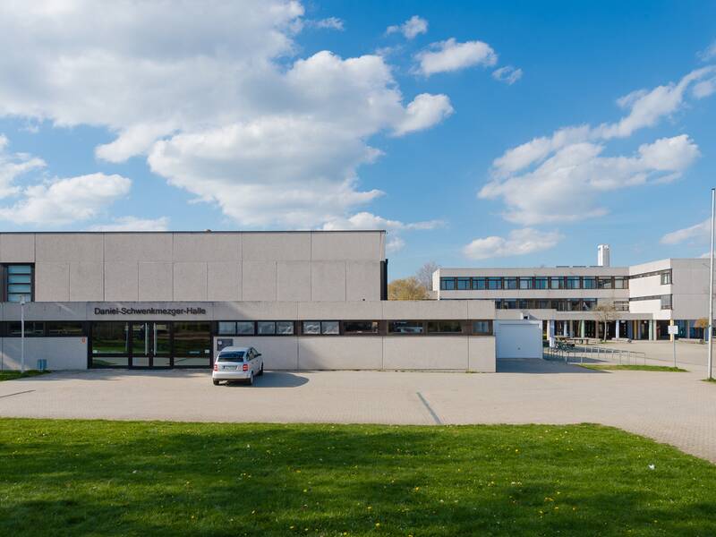 Bilder der Daniel-Schwenkmetzger-Halle in Laichingen, geschossen von vorne. Gesehen wird die Eingangstür, sowie im Hintergrund Teile des naheliegenden Gymnasiums