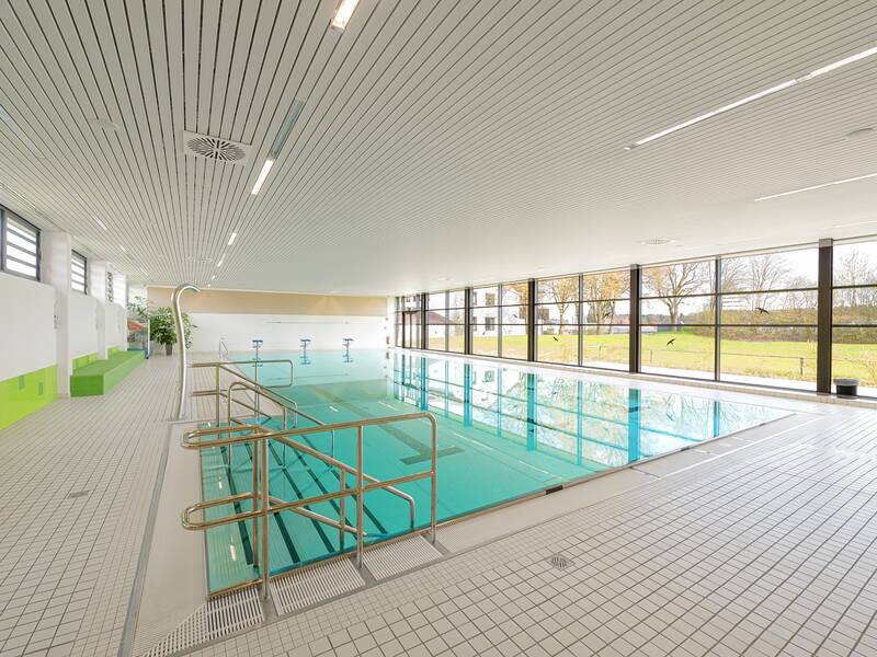 Ein modernes Hallenbad mit klaren Linien und großen Fenstern, die den Blick auf eine grüne Außenanlage freigeben.