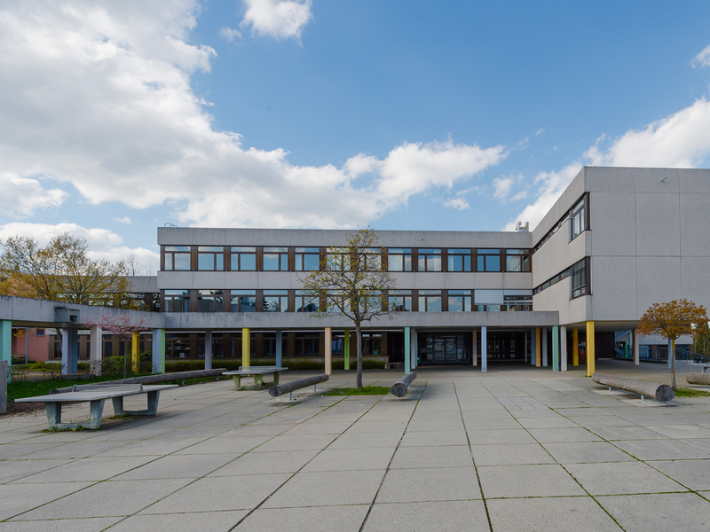 Schulhof des Gymnasiums mit Tischtennisplatten und großen Baumstämmen als Sitzgelegenheit
