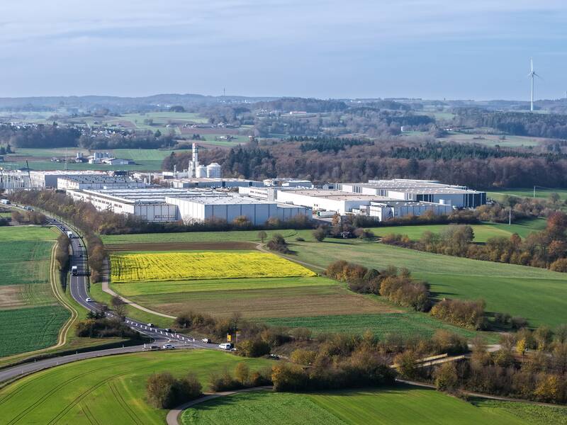 Ein Luftbild von Laichingens Industriegebiet, welches inmitten einer grünen, hügeligen Landschaft mit Feldern, Straßen und Windrädern am Horizont liegt.