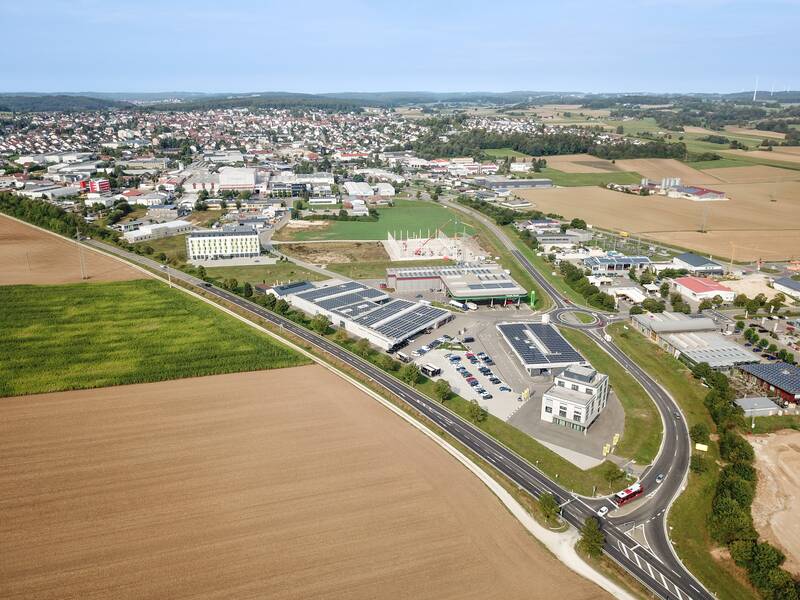 Luftaufnahme von Laichingen mit Feldern im Vordergrund, einer Straße, die sich durch ein Gewerbegebiet zieht und einer Siedlung im Hintergrund.