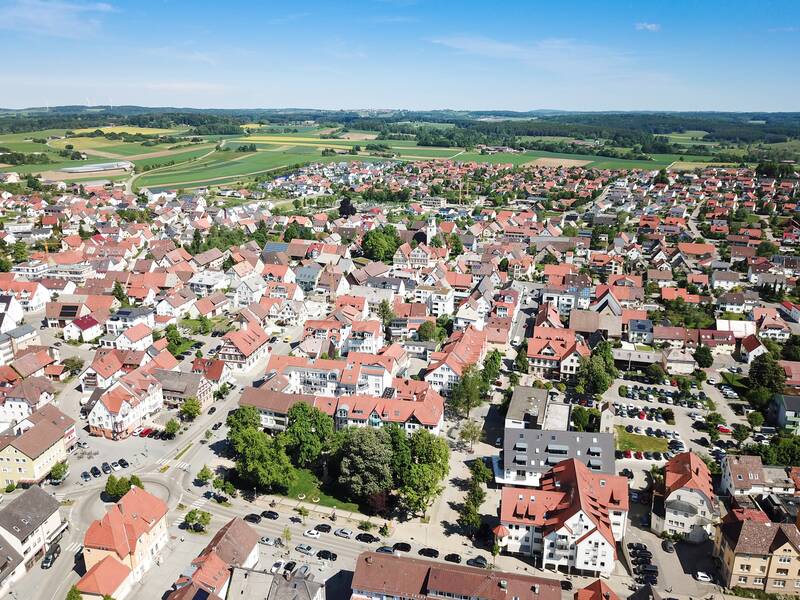 Eine Luftaufnahme zeigt Laichingen, die weitläufige Kleinstadt mit zahlreichen Häusern, roten Dächern, Parkplätzen und umliegenden grünen Feldern.