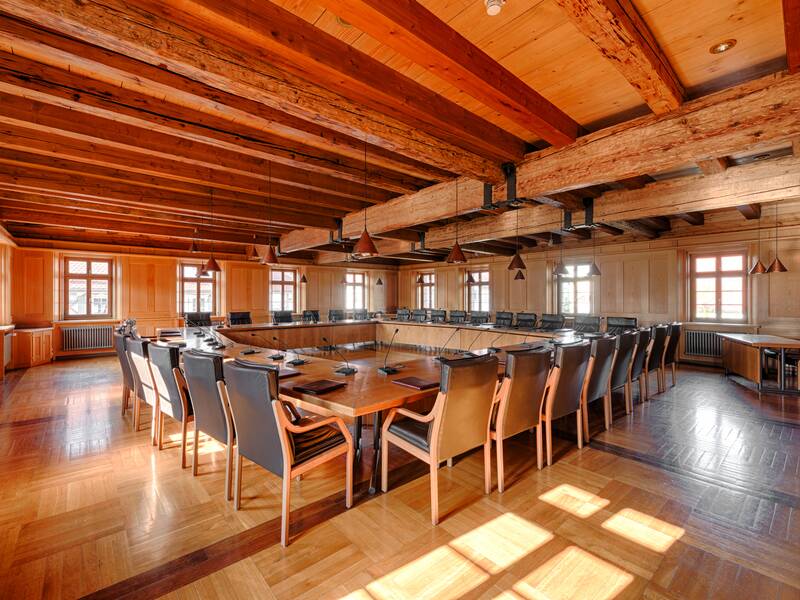 Ein großer, rustikaler Konferenzraum mit Holzbalkendecke, langen Holztischen und gepolsterten Stühlen.