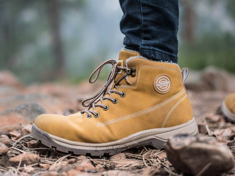 Ein beiger Wanderschuh steht auf einem steinigen Weg in einer natürlichen Umgebung.